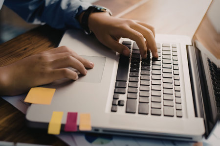 A person typing on a laptop with sticky notes on the side, focusing on work or study.