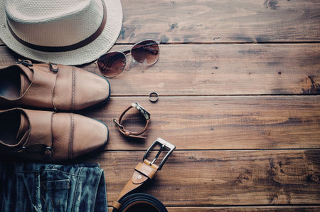 A selection of men's accessories including shoes, a hat, sunglasses, and a watch laid out on a...