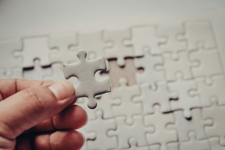 A hand holding a puzzle piece with a completed puzzle in the background.