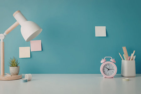 A well organized desk with office supplies, including a lamp, plant, clock, and cup with pencils,...