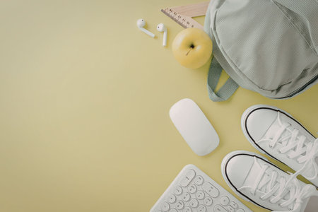 A green background with a backpack, earbuds, computer mouse, keyboard, and white sneakers.