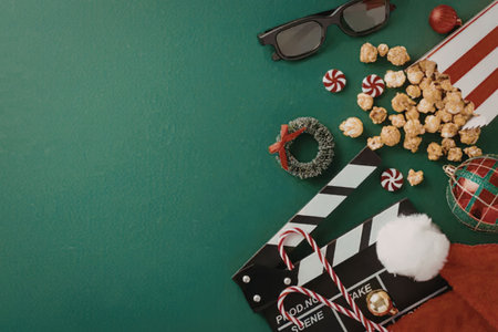 A festive arrangement of Christmas movie night essentials, including a clapperboard, popcorn, candy canes, and ornaments on a green background.の写真素材