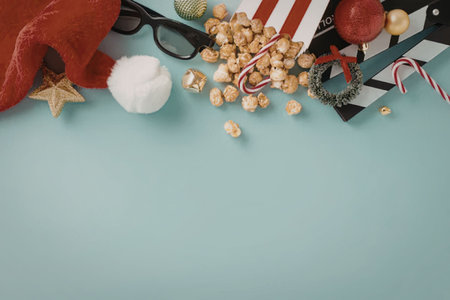 A festive arrangement of Christmas movie night essentials, including a Santa hat, popcorn, candy canes, and film reels on a light blue background.の写真素材