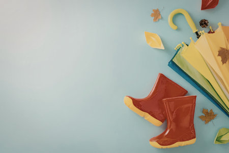A pair of red rain boots with yellow trim and a collection of colorful umbrellas and autumn leaves on a light blue background.の写真素材
