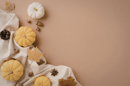A seasonal arrangement featuring small pumpkins, autumn leaves, and acorns on a white cloth against...