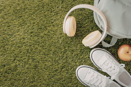 A pair of white sneakers, headphones and an apple on green grass