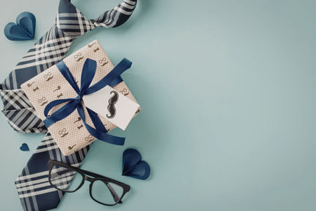 A gift box with a blue ribbon, plaid tie, glasses, and blue hearts on a light blue background.