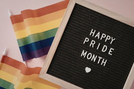 A colorful image featuring a letterboard with 'Happy Pride Month' and a rainbow flag on a pink...