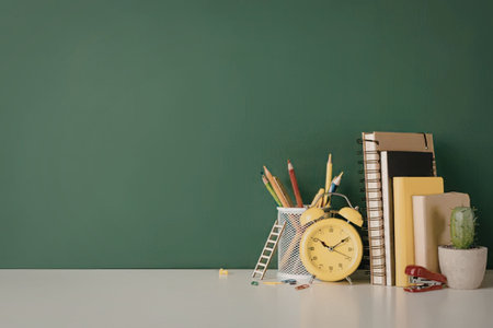A school desk with educational supplies, including books, pencils, a clock, and a cactus, against a...