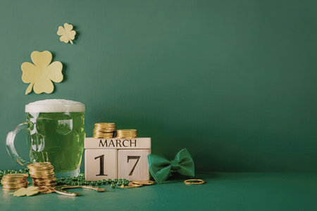 A festive St. Patrick's Day scene featuring a mug of green beer, a calendar marking March 17th, gold...