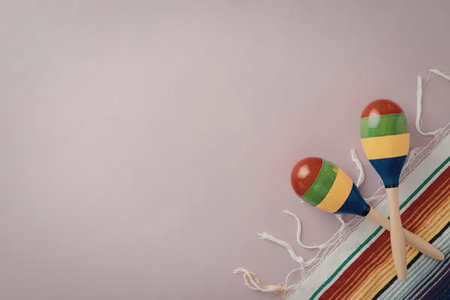 Two maracas with red, green, yellow, and blue stripes sit on a multicolored fabric against a pink...