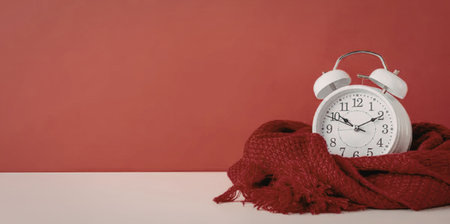 A white alarm clock sitting on a red scarf against a red wall