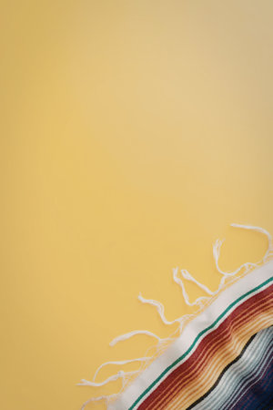 A colorful striped fabric with white fringe is placed on a bright yellow background, showcasing a...