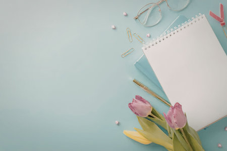 A serene writing desk setup featuring pink tulips, a notepad, glasses, and stationery on a light...
