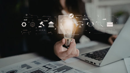 Business professional holding a glowing lightbulb with digital icons and graphs superimposed,...
