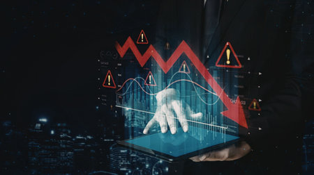 Businessman analyzes financial data on tablet with warning signs and graphs showing market decline and potential business crisis in a cityscape at night.の写真素材