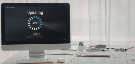 Computer monitor shows software update progress on a modern office desk surrounded by office supplies and documents.の写真素材