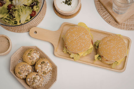 Burgers and salad artfully arranged on wooden trays and woven placemats on a clean white table...