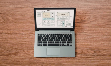 Laptop computer displays architectural floor plans on its screen, resting on a wooden table with a...