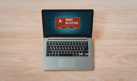 Laptop computer displaying a virus detected alert on its screen showing a red warning sign with a skull symbol on a wooden table surface.の写真素材