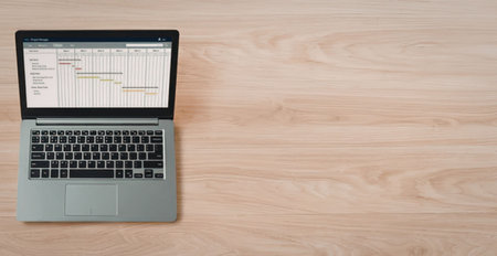 Modern laptop on a wooden desk displaying a line graph on its screen with colored lines and data...