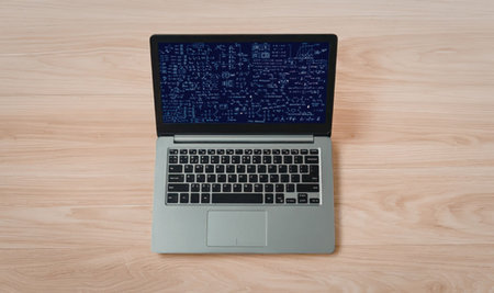Modern silver laptop displays code on a blue screen resting on a light wooden tabletop surface...