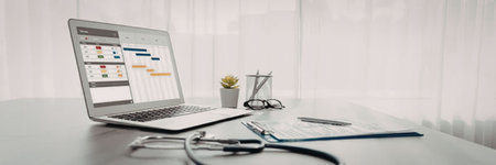 Laptop displaying a schedule or calendar on a clean white desk surrounded by medical equipment,...