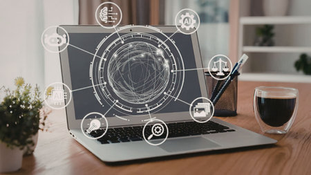 Laptop on wooden desk displays futuristic interface with icons and graphics surrounded by coffee and...