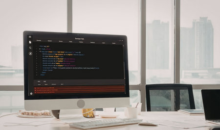 Modern office desk with a computer screen displaying coding software and a city view outside the...