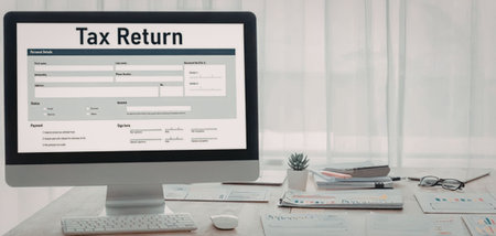 Computer monitor displays a tax return form on a cluttered office desk surrounded by papers,...
