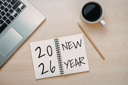 Notebook with 2026 new year written on it placed beside a laptop and coffee cup on a wooden desk.