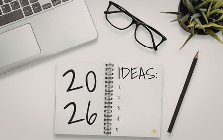 Open spiral notebook with ideas list and date on a clean white desk with a laptop and glasses nearby, symbolizing productivity and organization.の写真素材