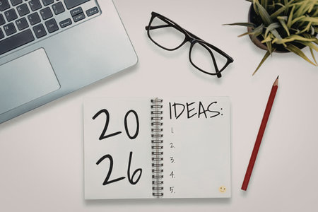 Notebook with ideas list lies on a white desk accompanied by a laptop and glasses, symbolizing a...