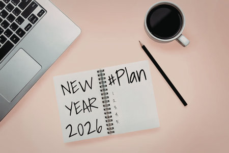 Notepad with new year plan 2026 on a peach desk with laptop and coffee cup nearby.