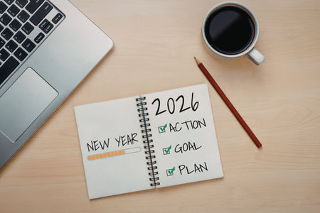 Notebook with new year 2026 and action, goal, plan checklist on a wooden desk with laptop and coffee...