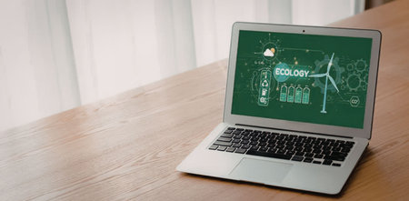 Silver laptop on wooden table displays green screen with ecology theme, featuring windmill and...