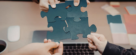 People collaborating and working together as a team fitting jigsaw puzzle pieces together over a...