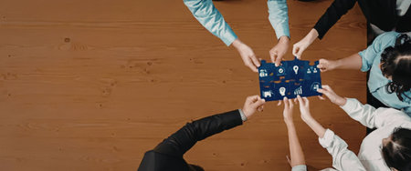 Business team assembles a blue puzzle with various business-related icons on a brown wooden table showcasing collaboration, teamwork, and unity in a corporate setting or office environment.の写真素材