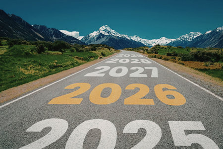 Empty asphalt road stretches through mountains marked with years leading up to 2026 under a clear blue sky, symbolizing journey, progress, and future goals.の写真素材