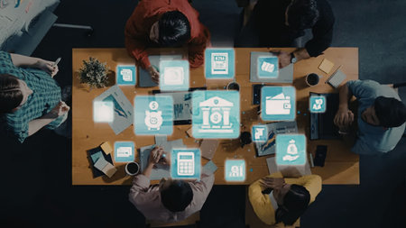 an overhead view of a group of people gathered around a large wooden table, each using a laptop or...