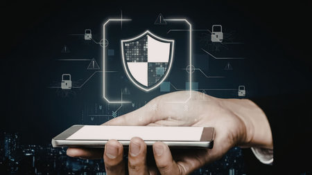 A hand holding a mobile device with a shield icon and various security symbols surrounding it,...