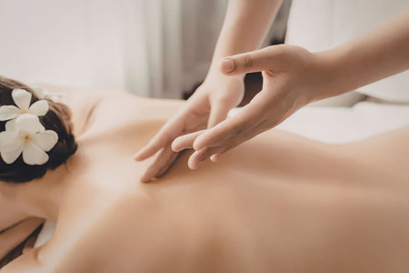 A woman lies on her stomach with a white flower in her hair as a person gives her a back massage.