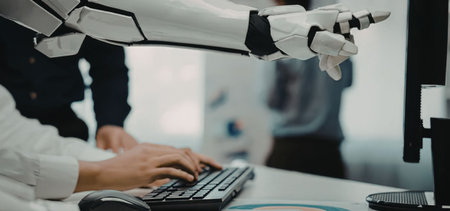 a close-up view of a robotic arm extending towards a computer monitor while a person interacts with...
