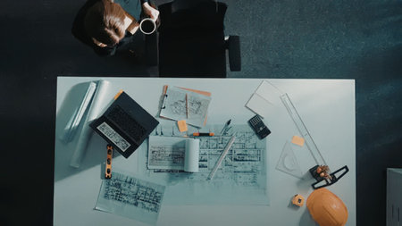 An overhead view of a white table with various tools and papers on it. A person is sitting at the...