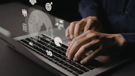 Business professional typing on laptop with global business icons and charts displayed above the...