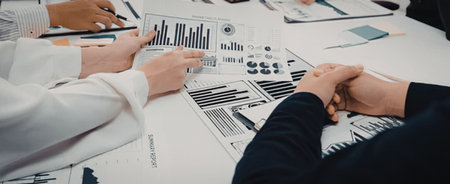 Business professionals gathered around a table reviewing and discussing various charts and data...