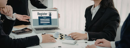 Business professionals gather around a laptop displaying an online registration form, actively...