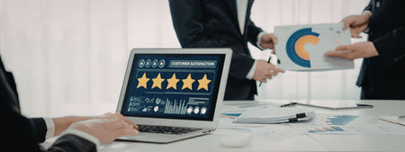 A business team in a meeting reviewing customer satisfaction ratings on a laptop, with a person...