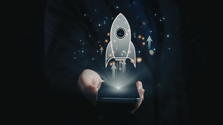 Businessman holding a smartphone with a rocket ship icon emerging symbolizing startup launch and...