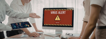 a group of colleagues gathered around a computer with a red screen displaying a virus alert and a yellow warning triangle, indicating a potential cyber threatの写真素材